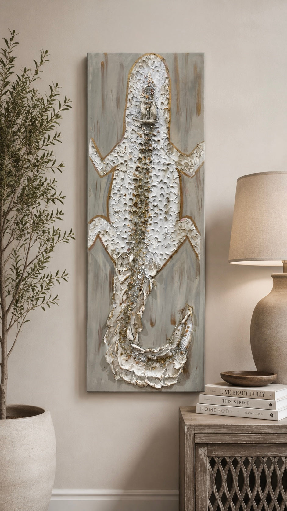 A vertical canvas wall art piece featuring a textured, raised alligator design in metallic silver and gold tones over a distressed gray wood-grain background, styled in a home decor setting next to a plant and a lamp.